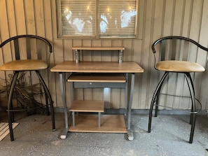 Un petit bureau en bois, doté de pieds en métal et d’une étagère, est placé entre deux chaises en métal à assise rembourrée, le tout adossé à un mur lambrissé en bois.