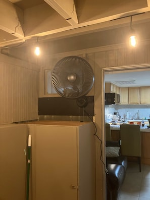 Eine kleine Küche mit integriertem Ventilator, einem Kühlschrank und einer Essecke mit einem Stuhl.