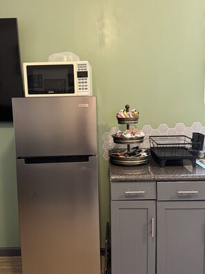 A kitchen with a stainless steel refrigerator, a microwave, a hexagonal tile backsplash, and a small dish rack.