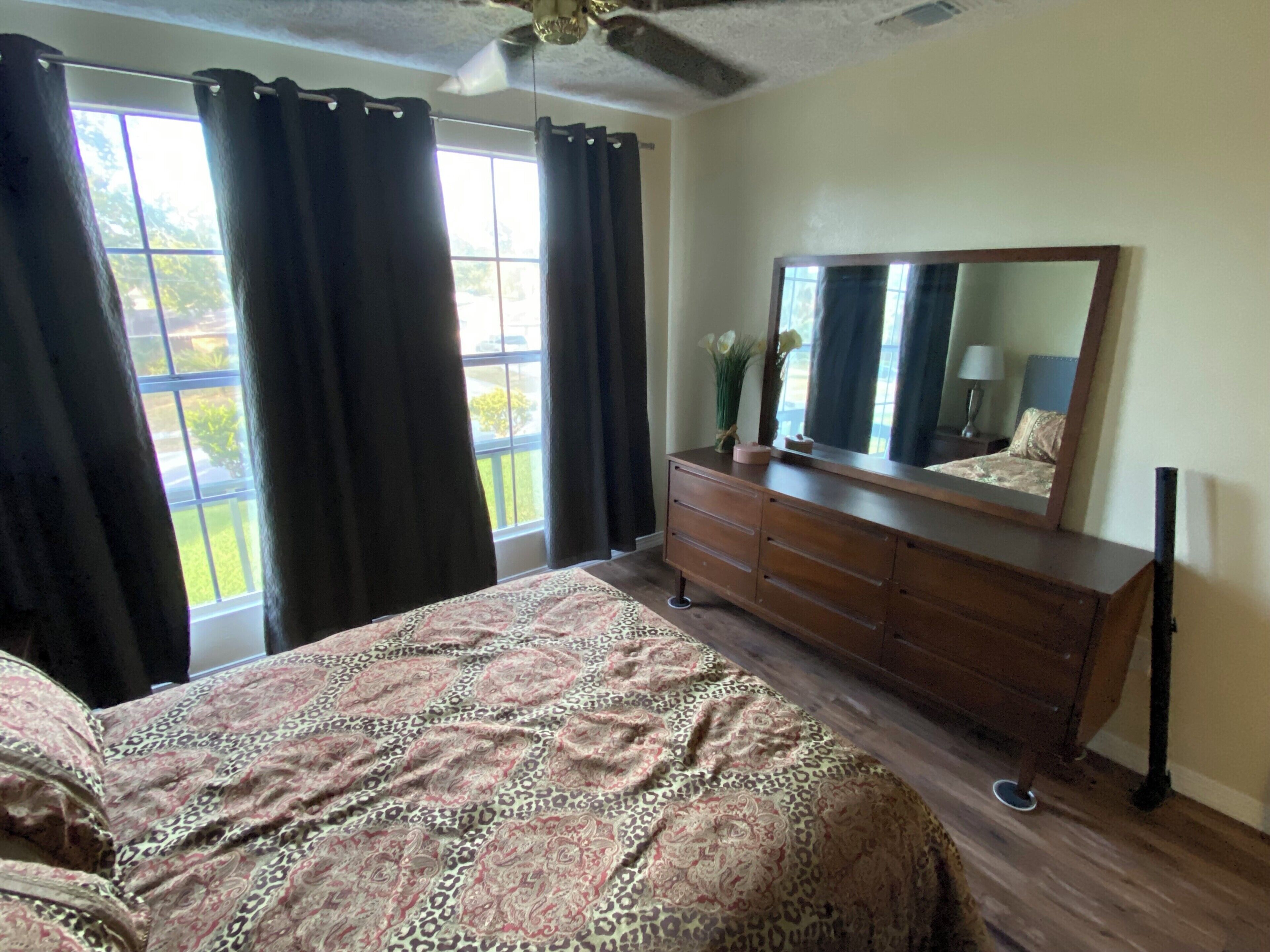 A bedroom with a bed, dresser, mirror, and windows with curtains.
