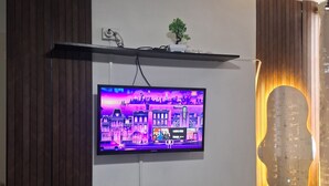 A television mounted on a wall with a cityscape display, a small plant on a shelf, and a decorative light fixture. - Spacious 3-bedroom apartment in tranquil Panamá with AC (Panamá)