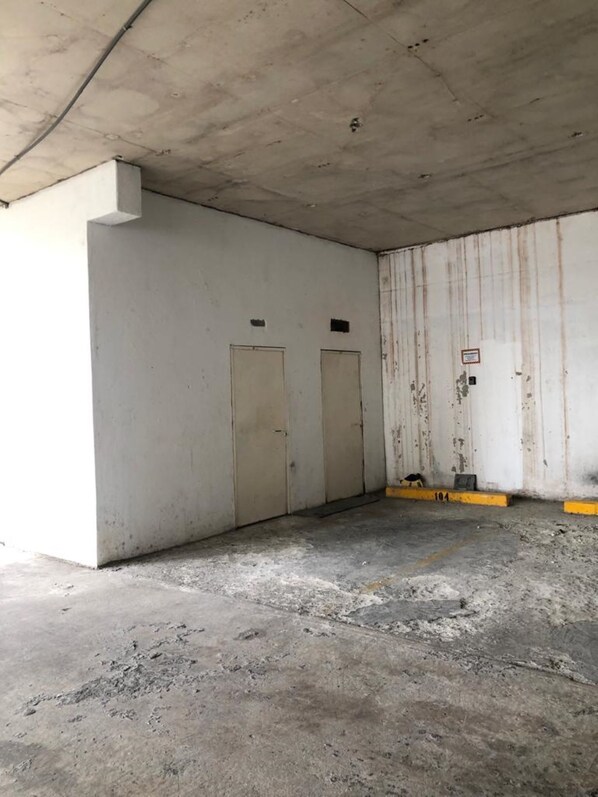 Una habitación vacía con pisos y paredes de concreto, dos puertas y una línea amarilla de seguridad.