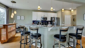 A kitchen with white cabinets, a central island with bar stools, a microwave, and a refrigerator. - Norfolk 5BR Family Home Near Ocean View Beach (Norfolk)