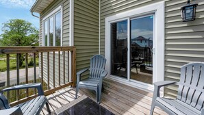 A covered deck with two Adirondack chairs, a wooden railing, and a sliding glass door leading to a patio. - Norfolk 5BR Family Home Near Ocean View Beach (Norfolk)
