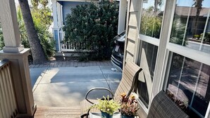 Eine Holzterrasse mit einem Stuhl und zwei Blumentöpfen, einem kleinen Tisch und einem Fenster mit Blick auf einen Garten.