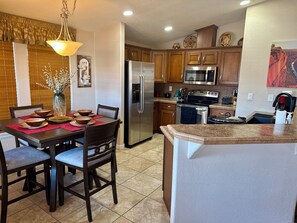 A kitchen with wooden cabinets, stainless steel appliances, and a dining area with a table set for four. - Palm Creek Resorts & Residences Charming 2-Bedroom 2-Bth Village House. (Casa Grande)