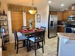 A kitchen with a dining table set for four, a refrigerator, microwave, and stove. - Palm Creek Resorts & Residences Charming 2-Bedroom 2-Bth Village House. (Casa Grande)