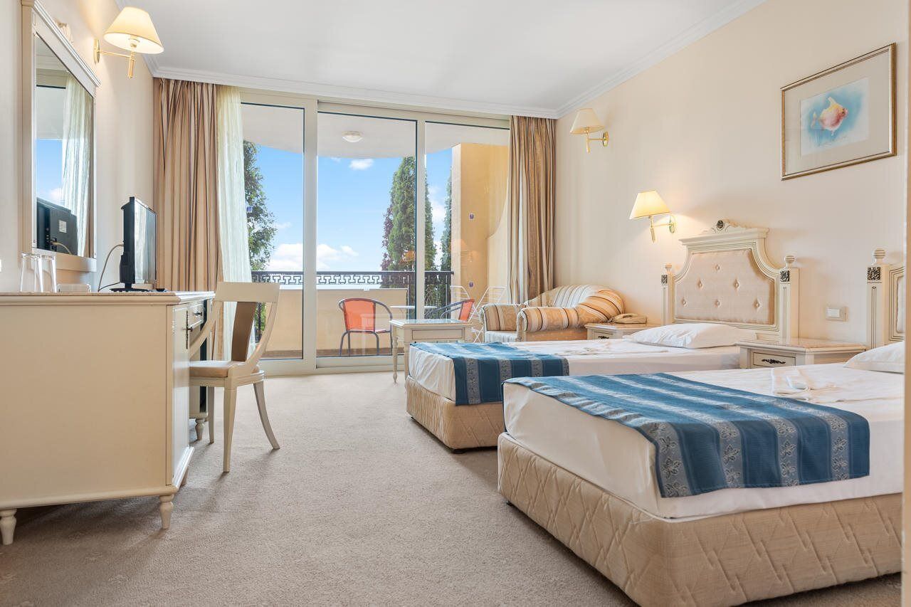A hotel room with two beds, a desk, a chair, and a view of the outdoors.