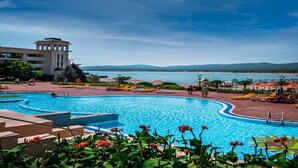 A swimming pool with a view of the sea, a building with a tower, and a clear sky. - Marina Royal Palace (Sozopol)