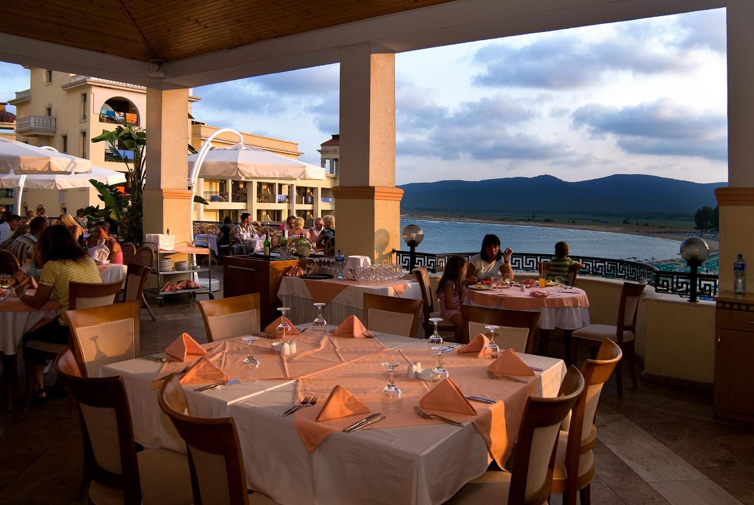 An outdoor dining area with tables set for guests, overlooking a body of water and mountains.