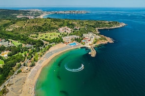 Ett flygbildsbild av en kustort med en strand, simbassänger och en småbåtshamn.