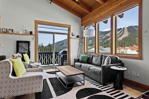 Un salon moderne avec un canapé, une table basse et une vue sur un paysage montagneux grâce à de grandes fenêtres.