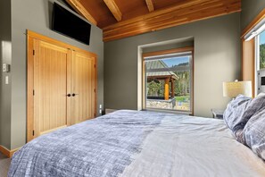Un dormitorio con una cama grande, un armario de madera y una ventana con vistas a un edificio y árboles.