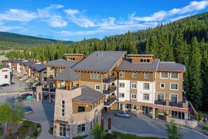 A multi-story hotel with a stone tower, balconies, and a view of a forested mountain.