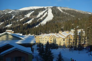 Una montaña nevada con un complejo de esquí en primer plano, que muestra edificios de varios pisos con balcones.