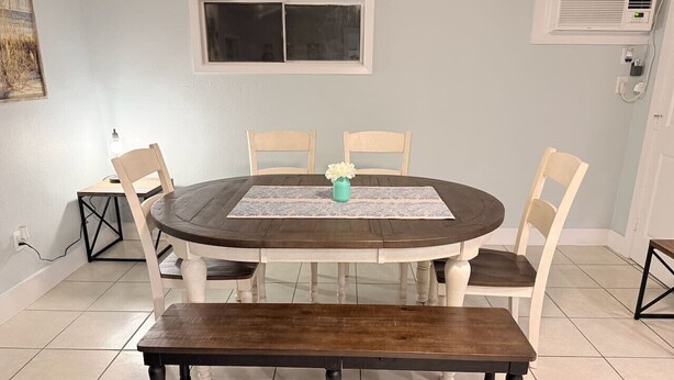 A round dining table with six chairs, a bench, a vase with flowers, and a window above. - Private Gated Montrose Cottage Near FIFA & Downtown (Houston)