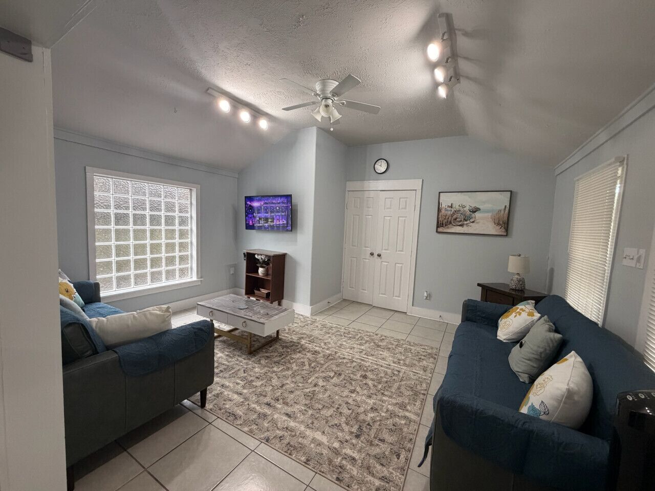 A living room with a ceiling fan, a TV, a clock, and a door.