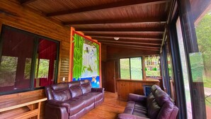 Interior de uma cabana de madeira com duas poltronas de couro, janelas amplas e um mural na parede.