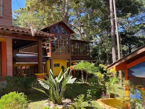 Una casa de dos pisos con balcón, rodeada de exuberante vegetación y árboles.