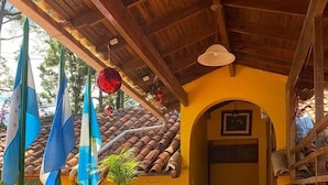 Uma área externa coberta com piso de azulejos, plantas em vasos e bandeiras.