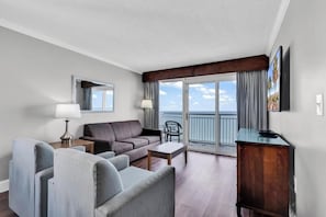 A hotel room with a balcony, a sofa, a chair, a table, and a TV. - Charming 3-bedroom condo with AC in lovely Myrtle Beach (Myrtle Beach)