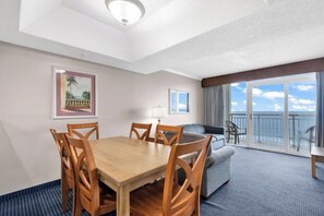 Ein Hotelzimmer mit Esstisch, Stühlen, einer Couch, einem Balkon mit Blick und einem gerahmten Bild an der Wand.