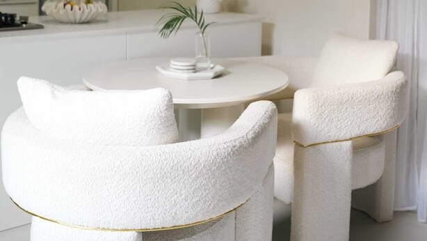 Een moderne, minimalistische kamer met een ronde tafel, twee witte stoelen, een vaas met bloemen en een grote spiegel.