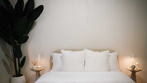 Een bed met witte beddengoed, twee nachtkastjes met lampen, en een grote potplant.