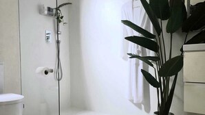 Een moderne badkamer met een douchecabine van glas, een toilet, een wastafel en een potplant.