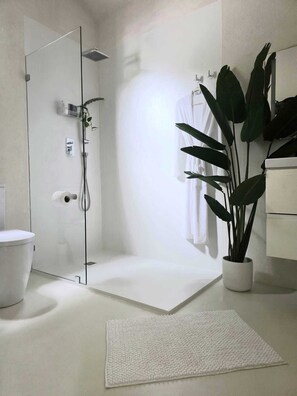 Ein modernes Badezimmer mit Duschkabine aus Glas, Toilette, Waschbecken und einer Topfpflanze.