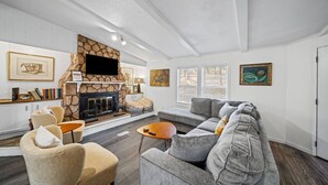 A living room with a stone fireplace, a grey sofa, a beige armchair, and a wooden coffee table. - Warm Days & Cool Knights—Fire Pit—Boat Rental! (Mooresville)
