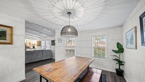 Ruime eethoek met een lange houten tafel, een hanglamp en uitzicht op een keuken en balkon.