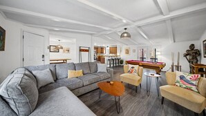 Een ruime woonkamer met een bank, fauteuils, een salontafel en een pooltafel.