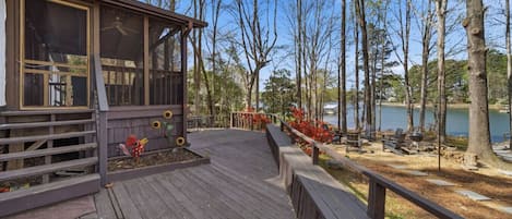 A wooden deck leading to a building with large windows, surrounded by trees and a lake.