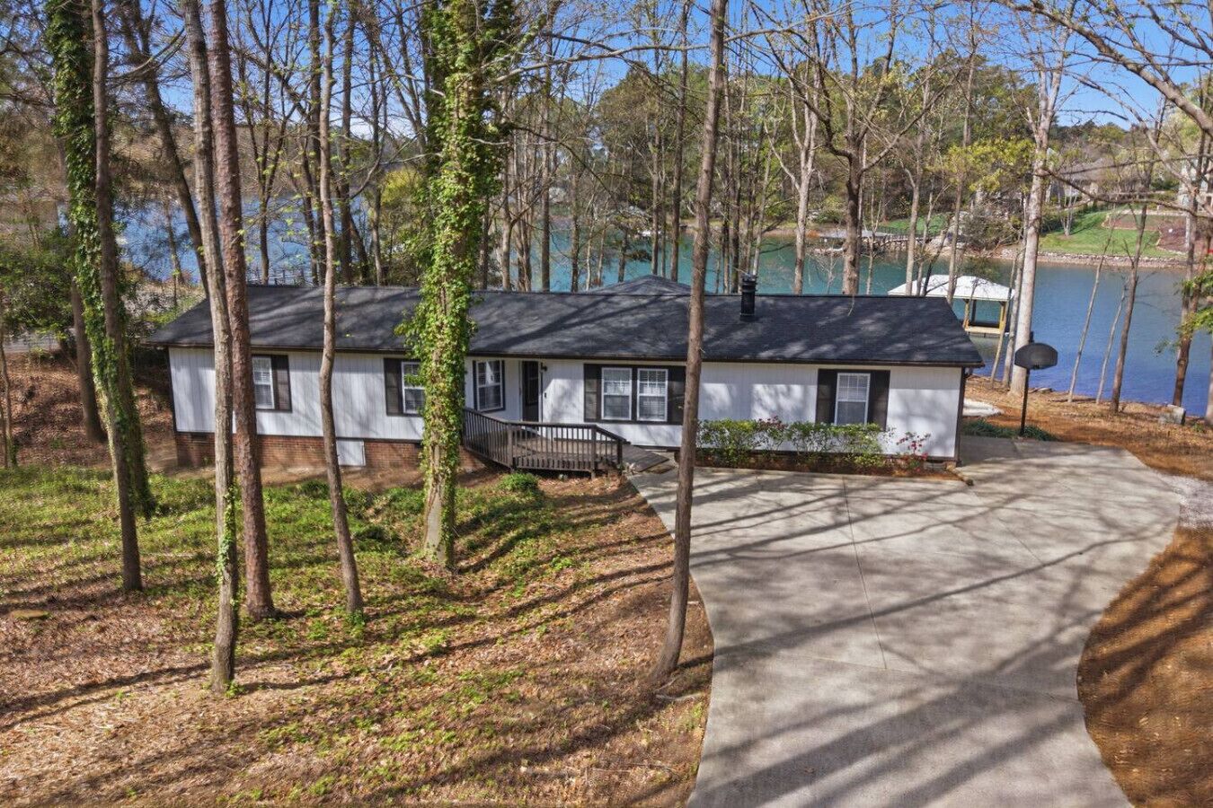 A single-story house with a front porch, surrounded by trees and a body of water.