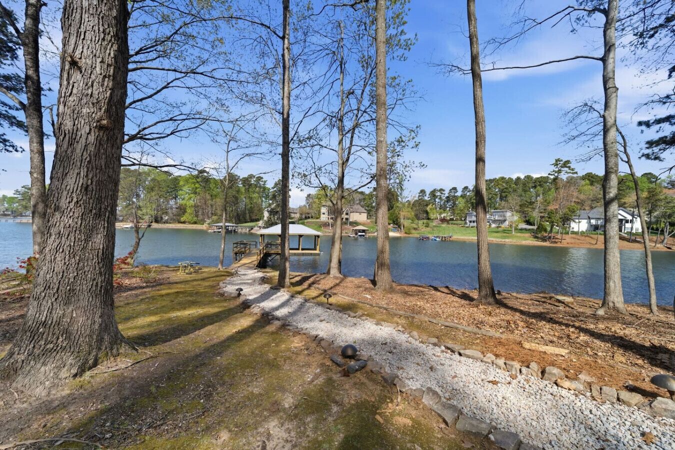 A lakeside view with a gazebo, trees, and a dock.
