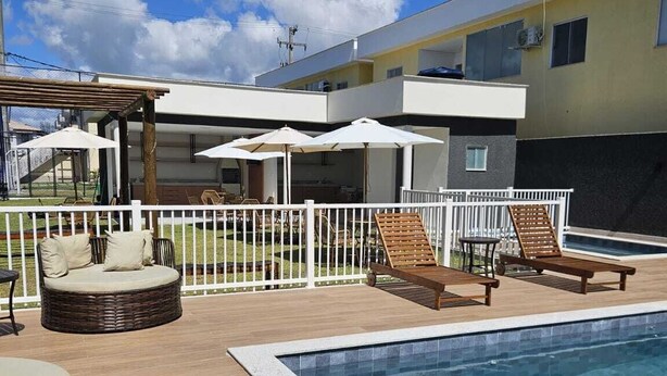 A poolside area with lounge chairs, umbrellas, and a wooden deck. - Apartment in a prime location on Coroa Vermelha beach, in a gated community. (Santa Cruz Cabrália)