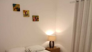 A neatly made bed with a green throw, a bedside lamp, and three wall art pieces. - Apartment in a prime location on Coroa Vermelha beach, in a gated community. (Santa Cruz Cabrália)