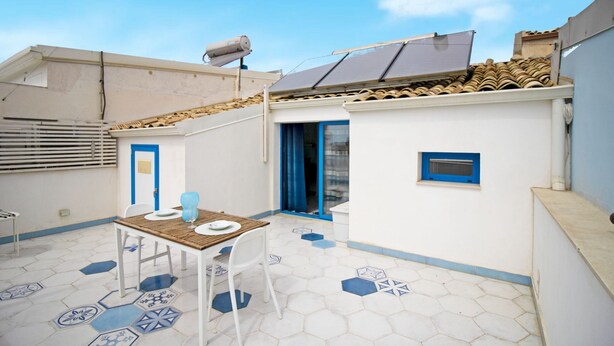 Een dakterras met een tafel, stoelen, een blauwe deur en een klein raam.