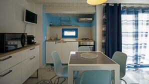 Een praktische keuken met een magnetron, kookplaat en spoelbak. Er is een eettafel met stoelen en een tv aan de muur bevestigd.