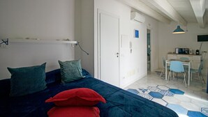 Een slaapkamer met een bed, kussens, een bureau en een stoel in een gang.