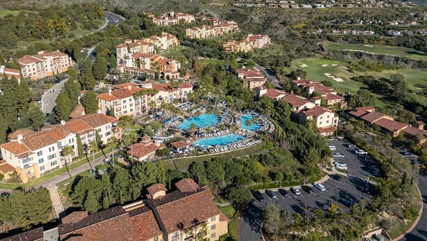 Luftaufnahme eines Resorts mit mehreren Gebäuden, einem zentralen Poolbereich und umliegender Bepflanzung.