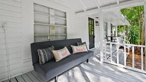 A covered porch with a dark gray sofa, two pillows with text, and a white railing.