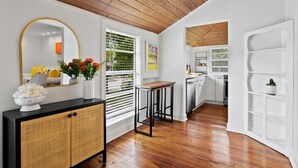 A modern kitchen with white cabinetry, a wooden ceiling, and a dining area with a black table and chairs.