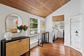 Una cocina moderna con armarios blancos, techo de madera y zona de comedor con mesa y sillas negras.