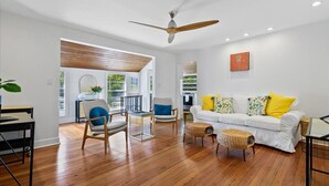 A modern living room with a white sofa, wooden flooring, and a ceiling fan.