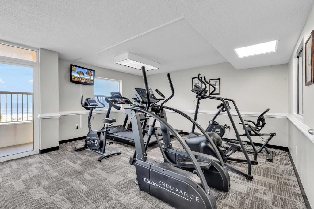 A gym with treadmills, elliptical machines, and a TV on the wall.