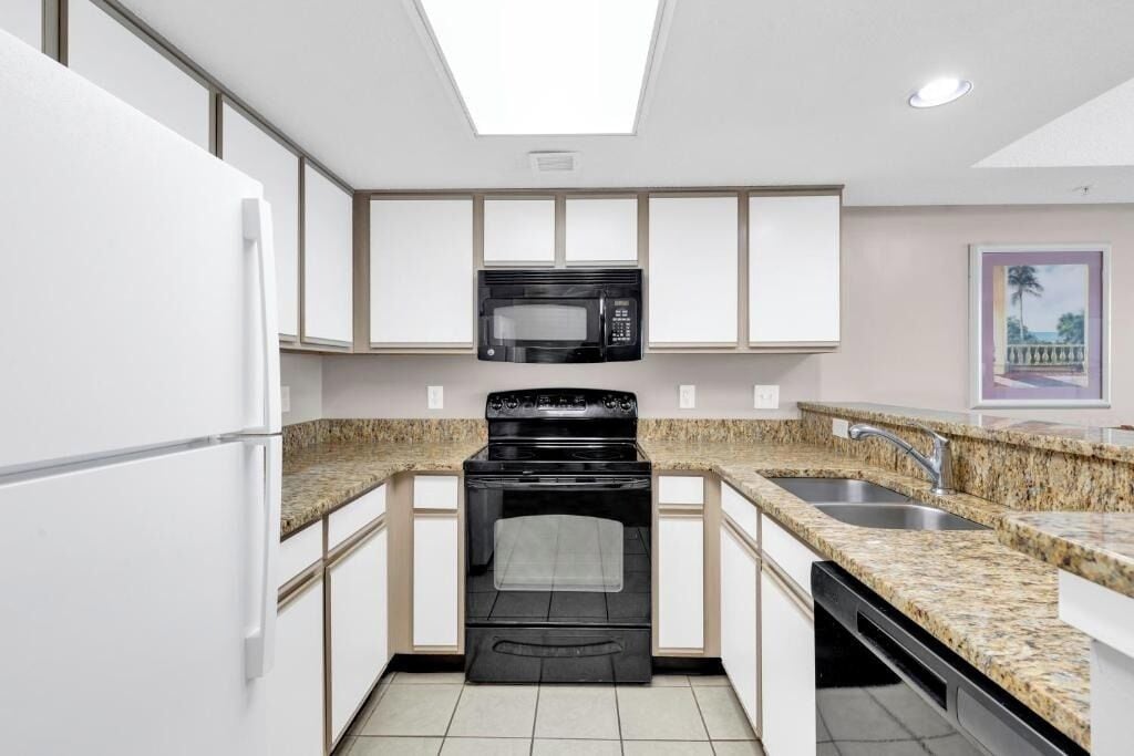 A modern kitchen with white cabinets, a black stove, a microwave, granite countertops, and a tiled backsplash.