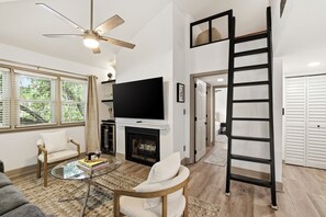 Una sala de estar con chimenea, televisor y una escalera.