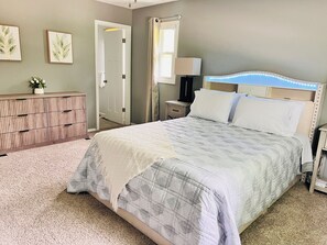 A bedroom with a bed, a dresser, a nightstand, and a door.